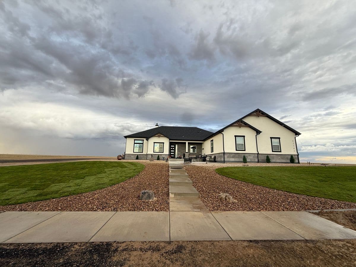 A finished front yard: two crescents of new sod, rock beds and a concrete walk leading to a new home under a wide sky.