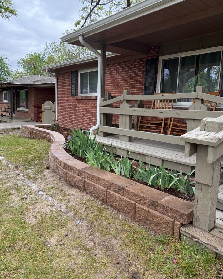 A curved block retaining wall forming a planted bed in front of a brick home.