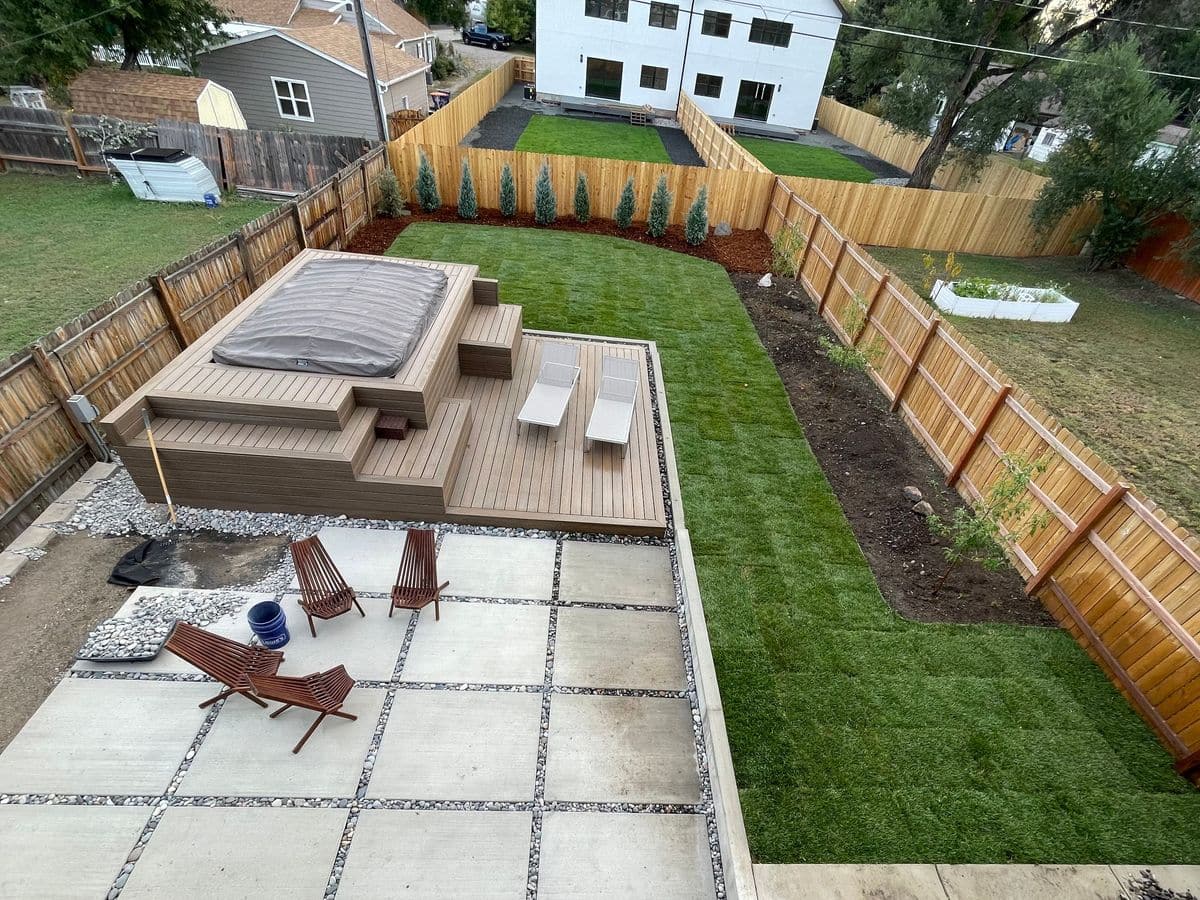 A finished backyard seen from above: concrete patio pads with gravel joints, a deck, new sod, a gravel border and a cedar fence.