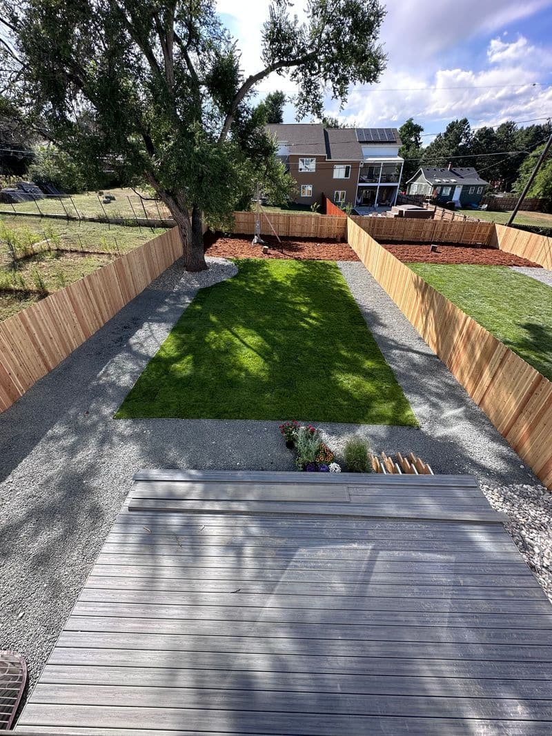 A long backyard with a strip of new sod between gravel borders, enclosed by a cedar fence.