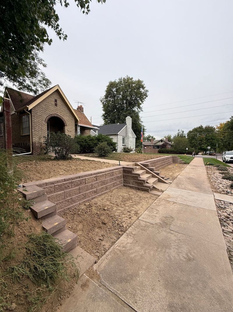 A terraced block retaining wall with steps beside a sidewalk.